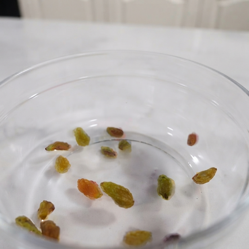 Raisins, walnuts, sliced almonds, and pumpkin seeds mixed together inside a transparent glass bowl.