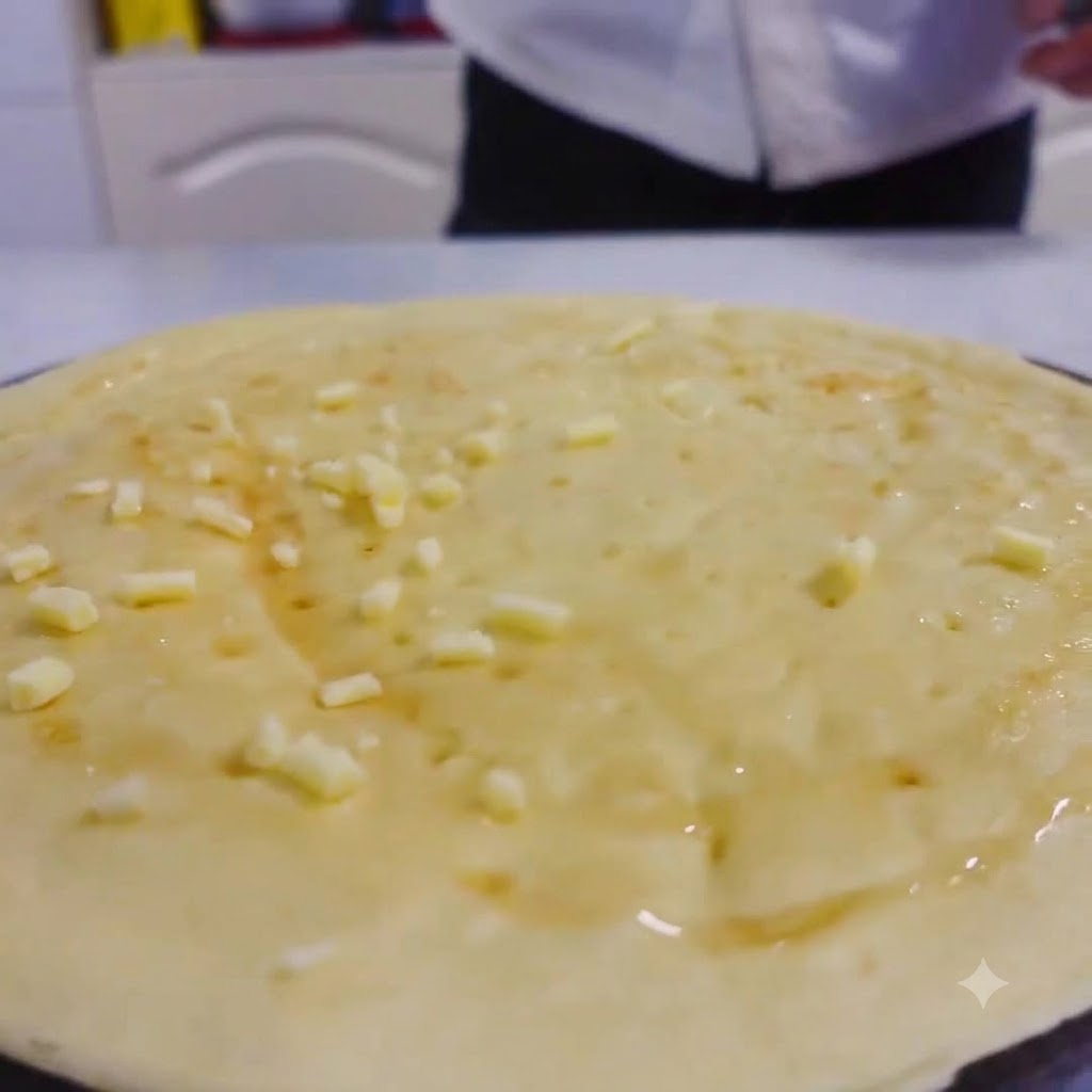 Shredded cheese scattered evenly over the honey-glazed surface of a pizza dough.