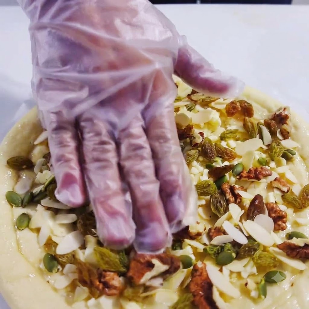 A gloved hand pressing down gently onto the fruit and nut toppings of a pizza.