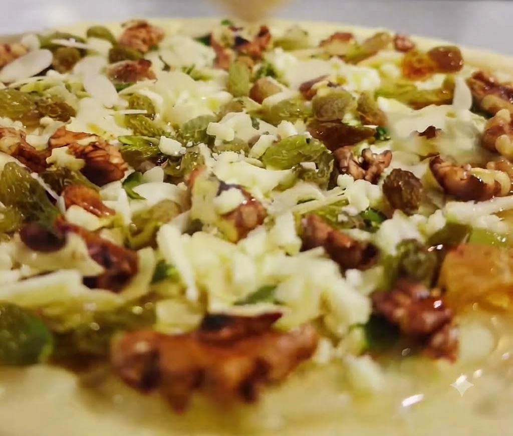 Shredded cheese being scattered over the top of the fruit and nut pizza layer using a brush or tool.