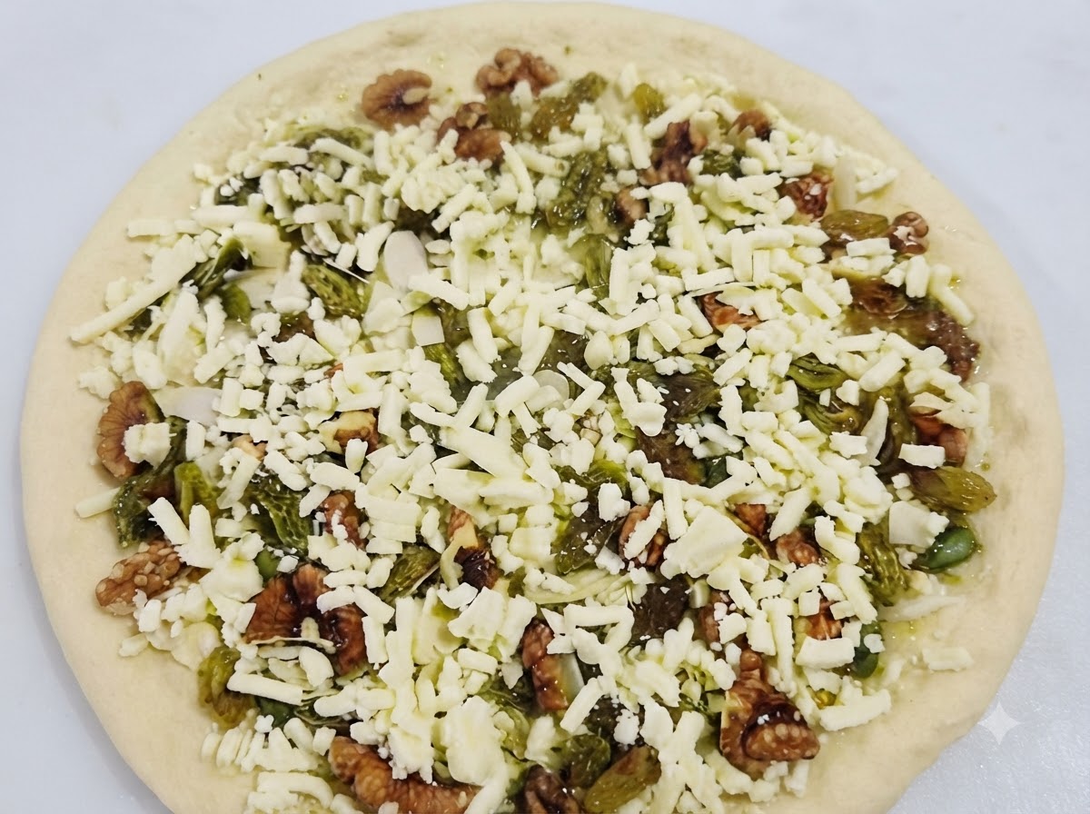 A fully assembled sweet pizza covered in cheese, walnuts, and raisins ready to be baked.
