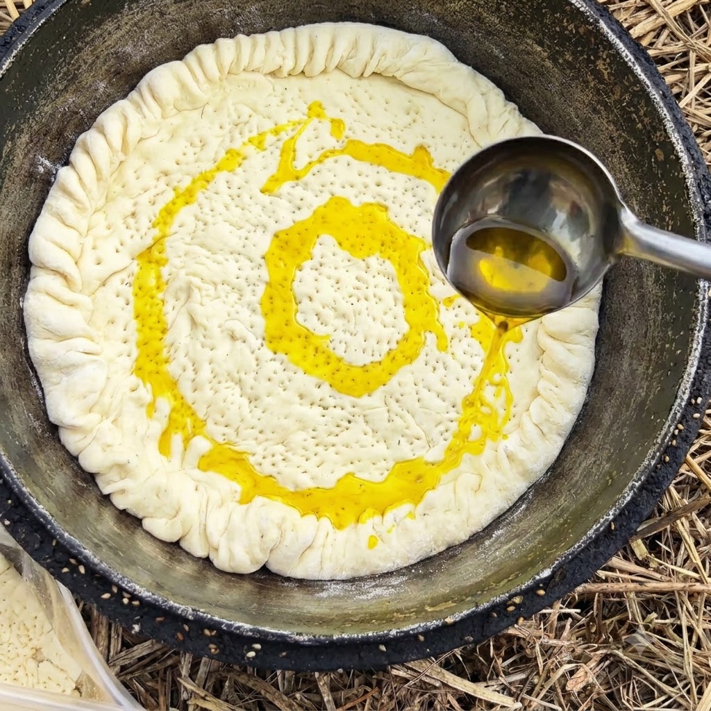 A metal ladle pouring yellow cooking oil over a dough crust inside a pot.