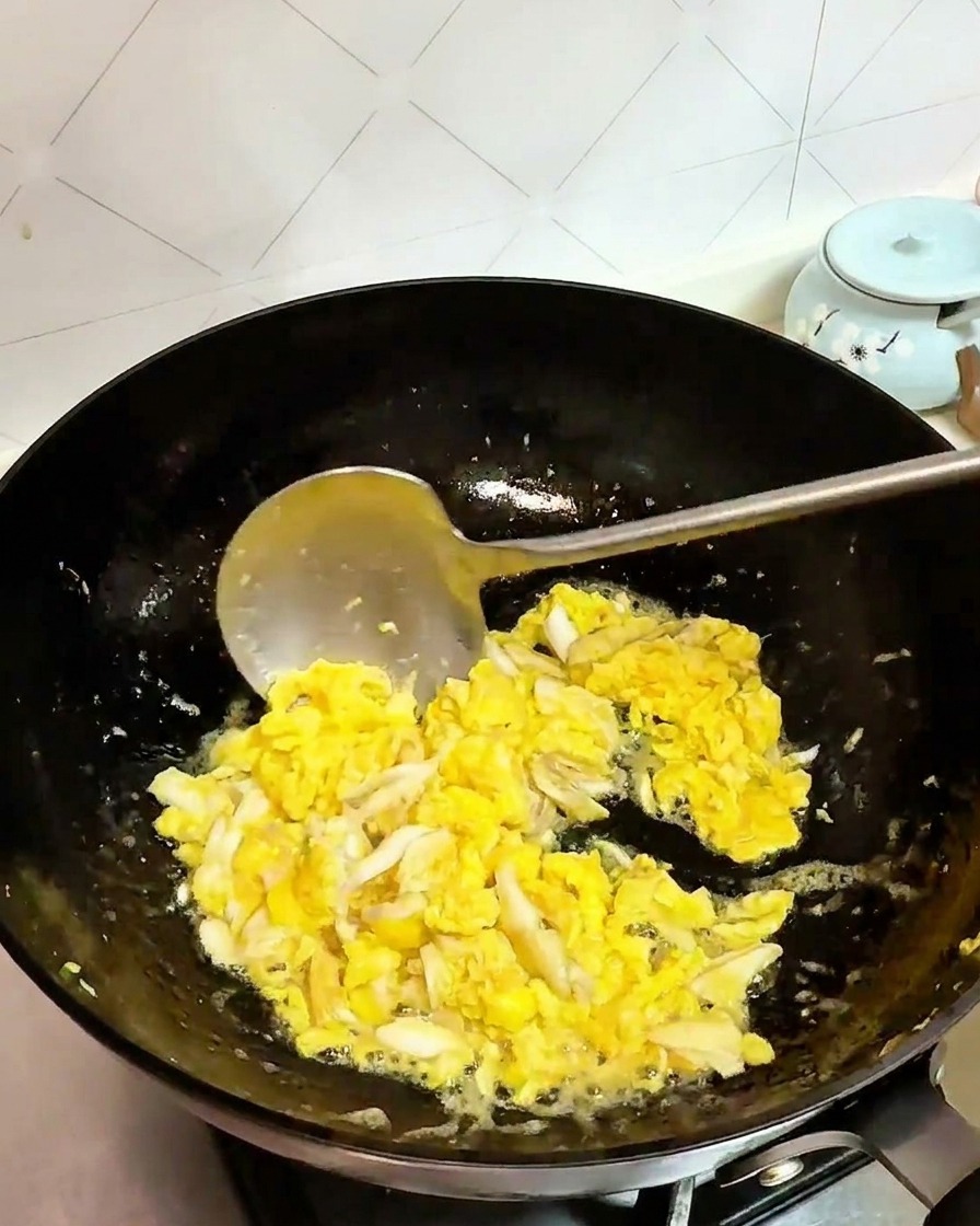 Crab meat and eggs being stir-fried together in a black wok with a ladle.
